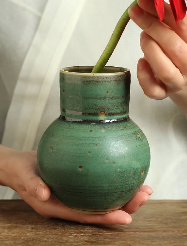Small sage green ceramic vase with speckles, holding a flower stem.