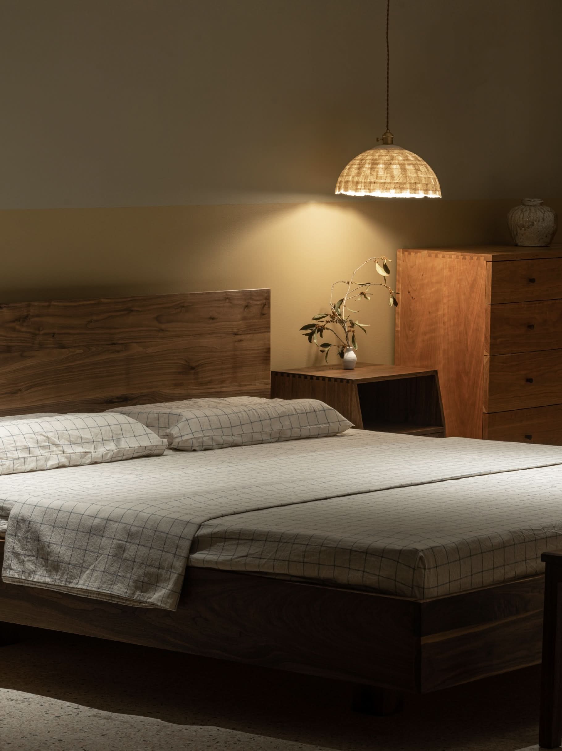 Woven paper mache lamp shade illuminates a cozy bedroom with a modern wooden bed.