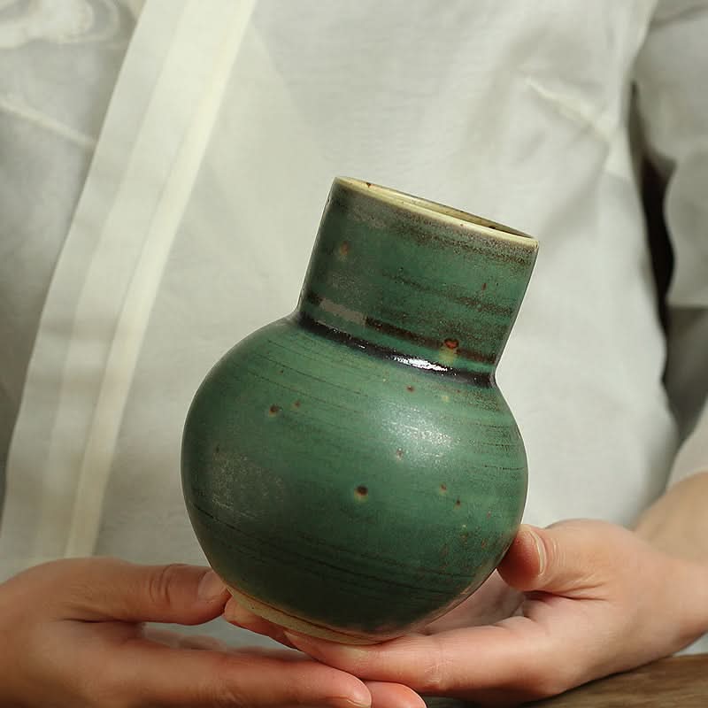 Small sage green ceramic vase with textured finish, held in hands, home decor.
