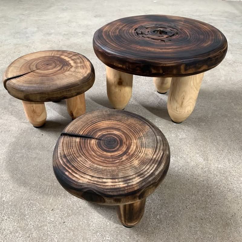 Rustic wood stools with charred tops and light wood legs, displayed on a concrete floor.