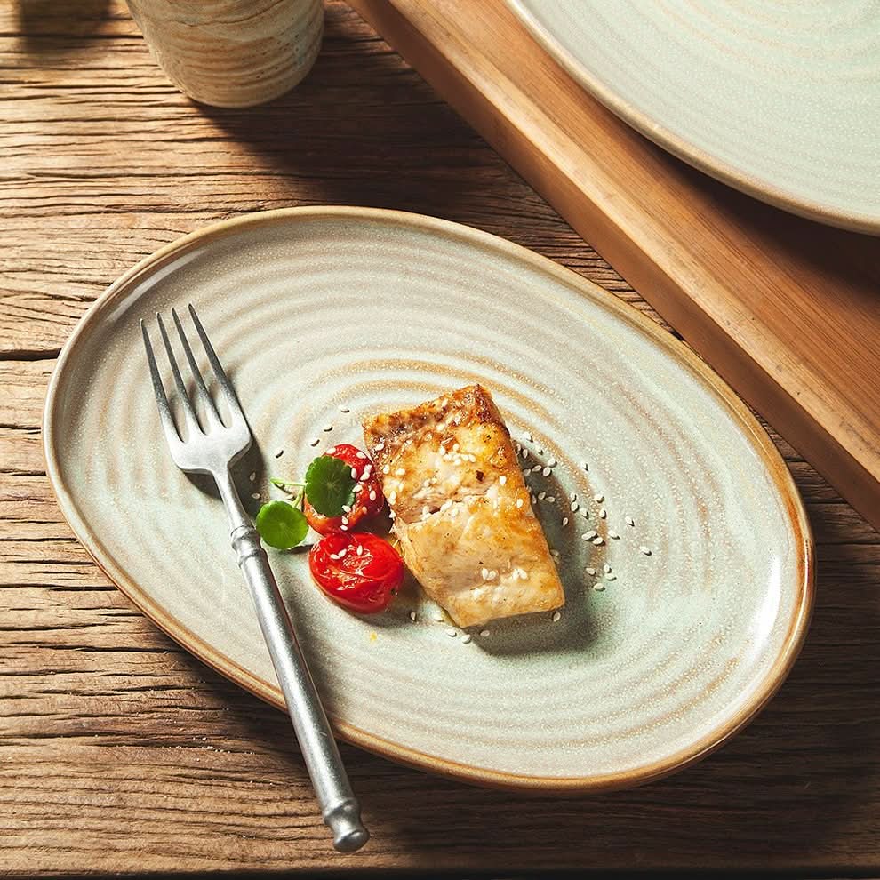 Rustic stoneware plate with food, featuring grey tones and a modern oval shape.