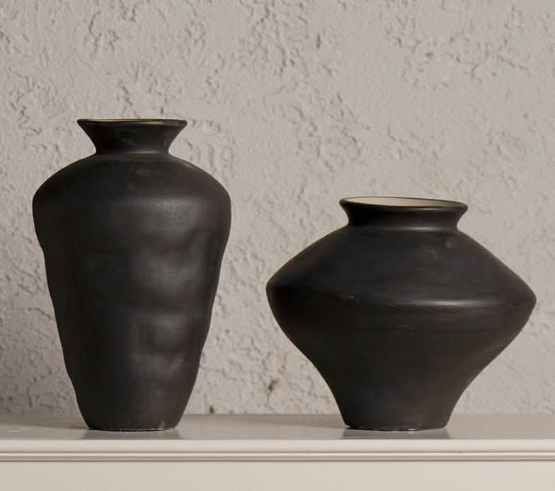 Two black ceramic irregular vases on a white shelf against a textured wall.