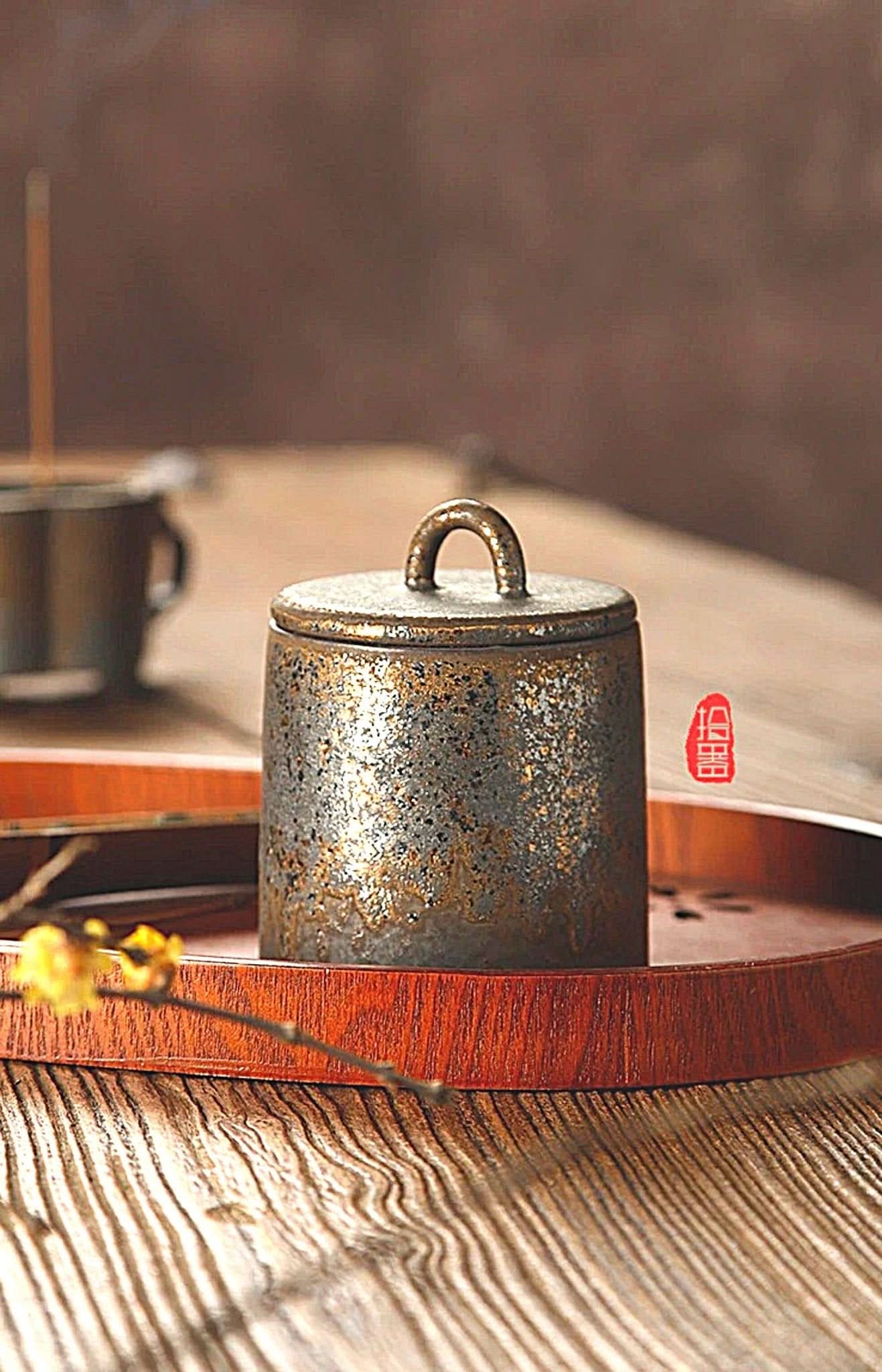 Rustic ceramic tea canister with metallic flecks, set on a wooden tray. Home decor.