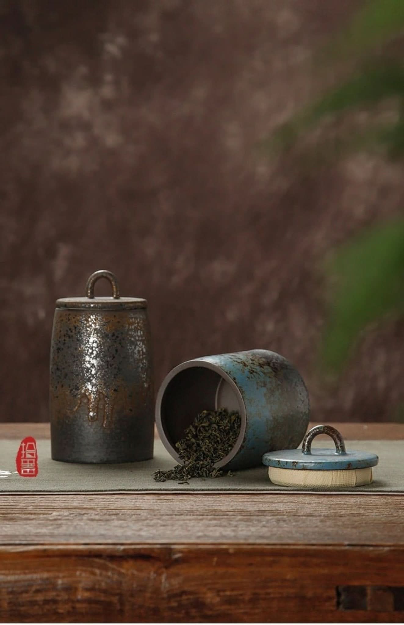 Rustic ceramic tea canisters with textured glaze and metal handles on a wooden surface.