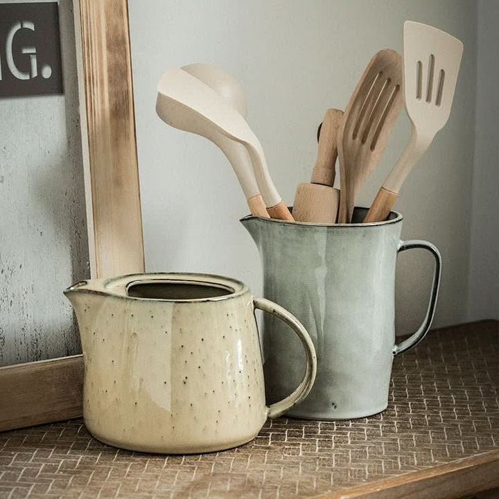 Cream speckled ceramic pitcher, gray utensil holder, farmhouse style.