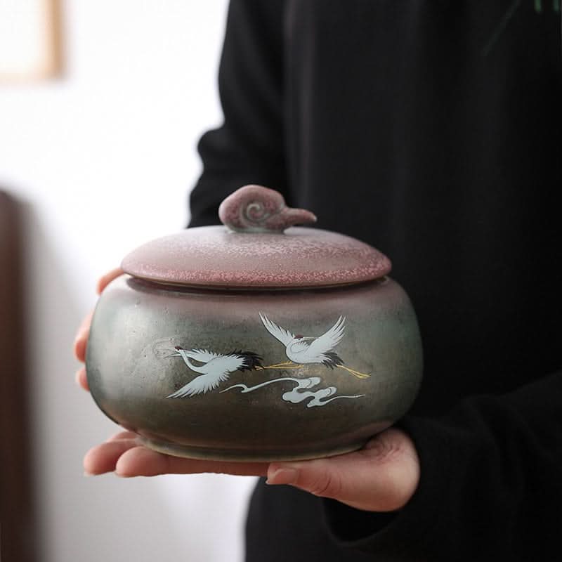Ceramic tea can with Japanese art illustration, held by hands. Storage jar for kitchen organization.