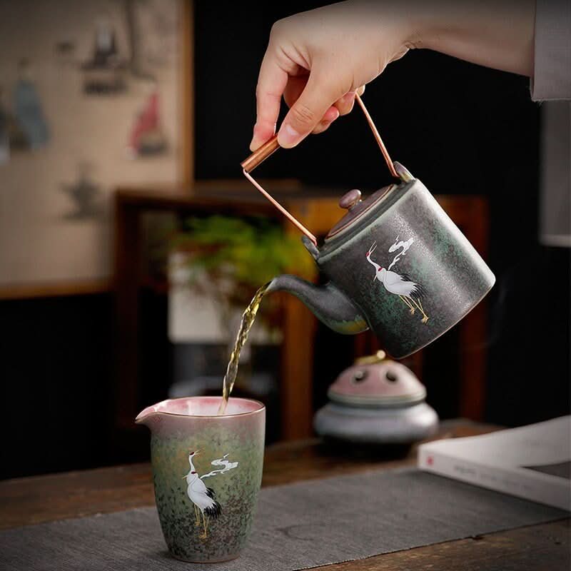 Ceramic tea pot with Japanese crane pouring tea into matching cup. Traditional Asian tea ceremony set.