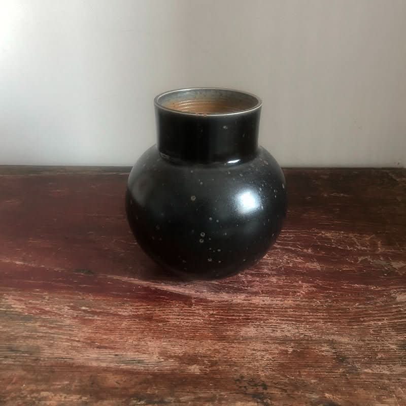 Clay handmade large vase, rounded black pottery with speckled finish on rustic wood.