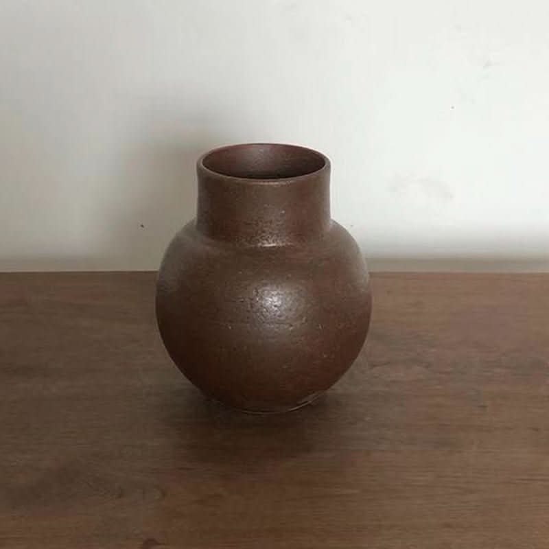 Clay handmade large rounded vase in a rich brown earthy tone, sits on a wooden surface.