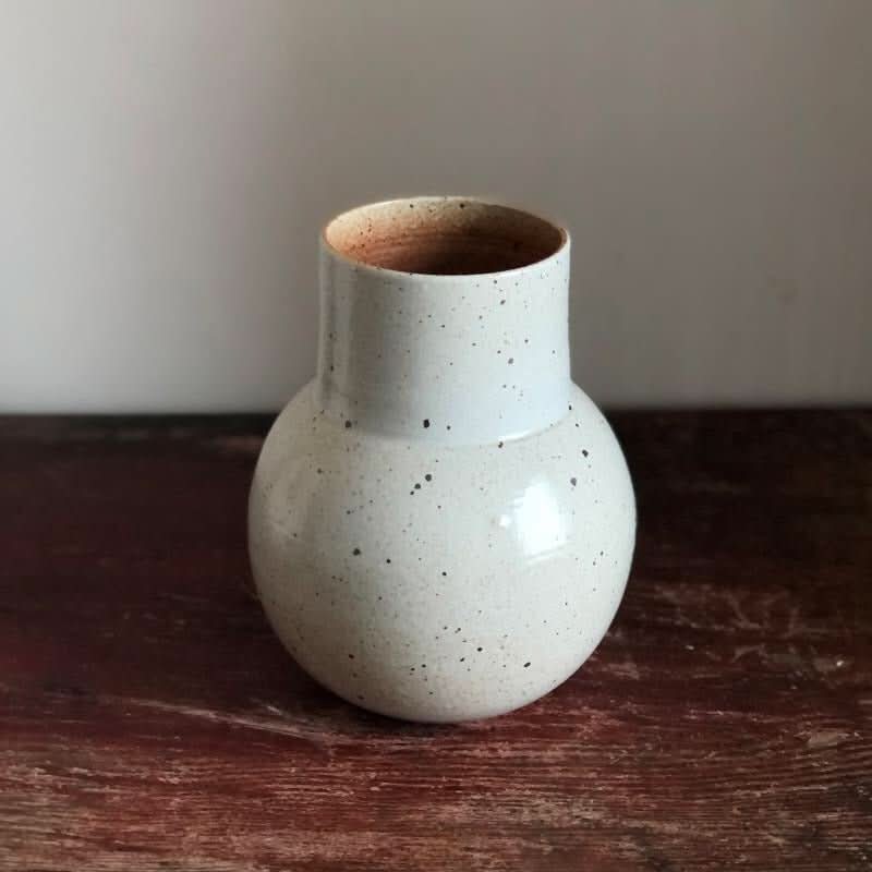 White speckled clay handmade large rounded vase on a wooden surface.