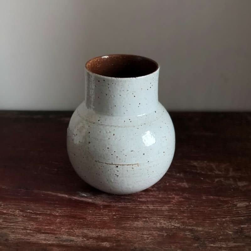 Speckled white clay handmade large vase with rounded shape and brown interior, on rustic wood.