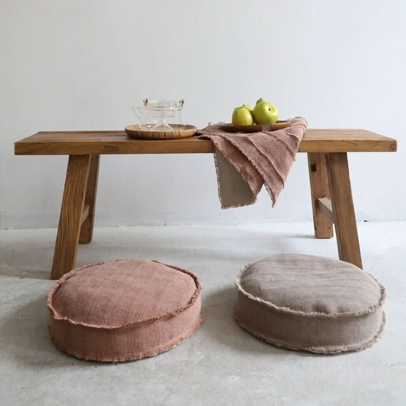 Cotton distressed meditation pillows in terra cotta and tan, on floor next to rustic bench.