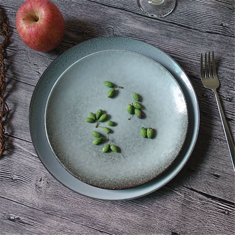 Cyan blue speckled ceramic dinnerware set with green berries and apple on rustic wood table.