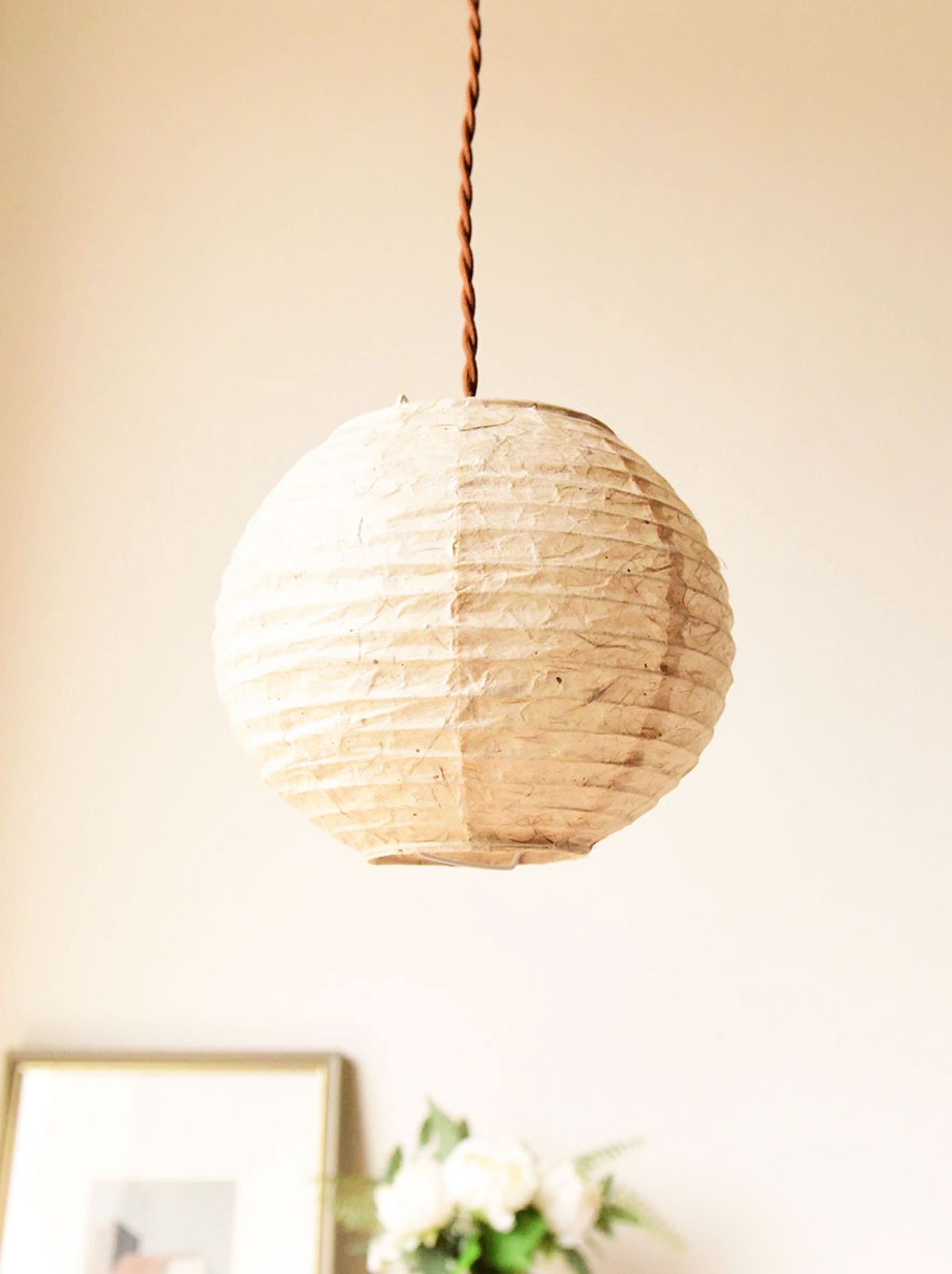 Textured beige handmade paper lampshade hanging with brown cord. Home decor.