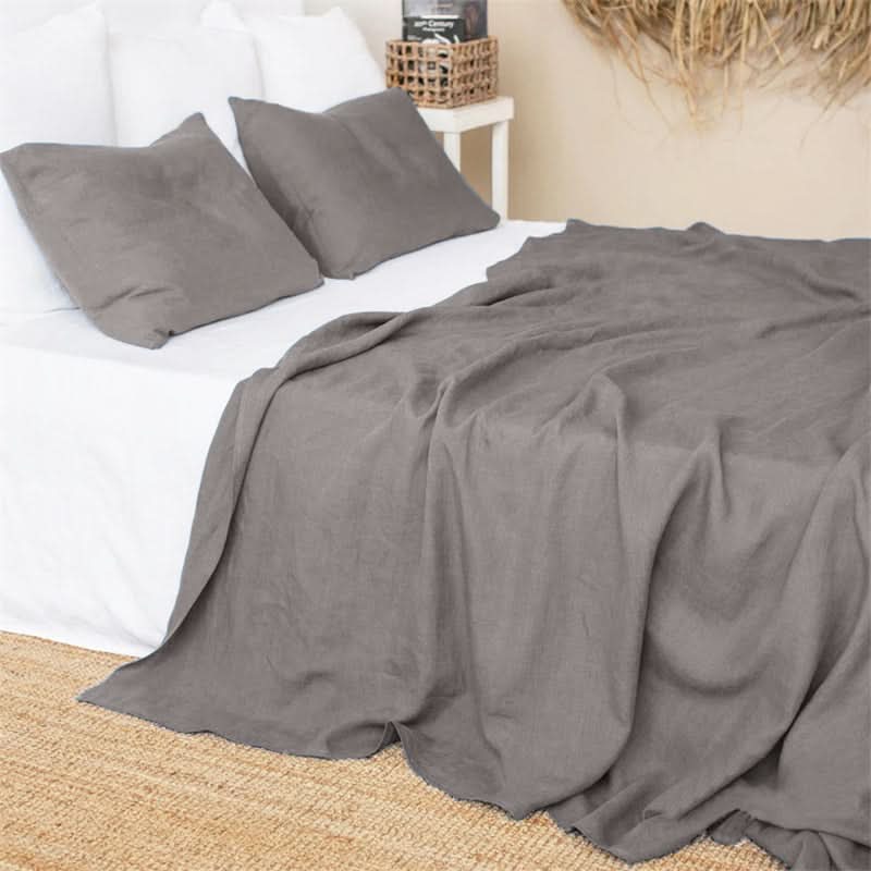 Grey linen bed sheets on a white bed with accent pillows and a woven basket.