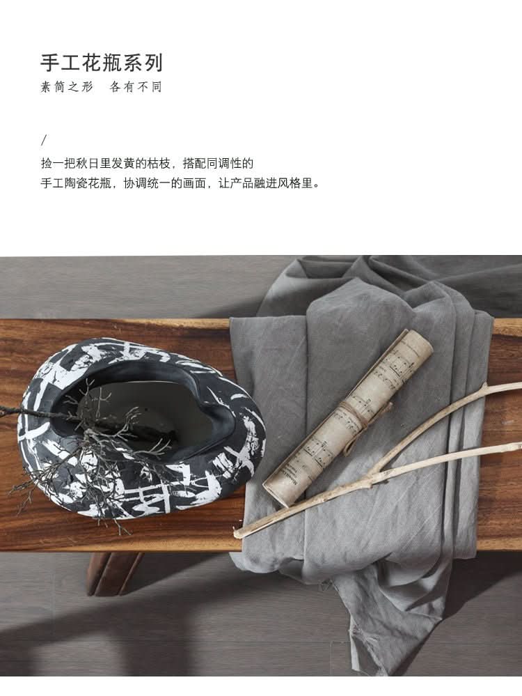 Handmade wabi sabi ceramic flower ware with black and white abstract art, on a wooden table, with branches and sheet music.