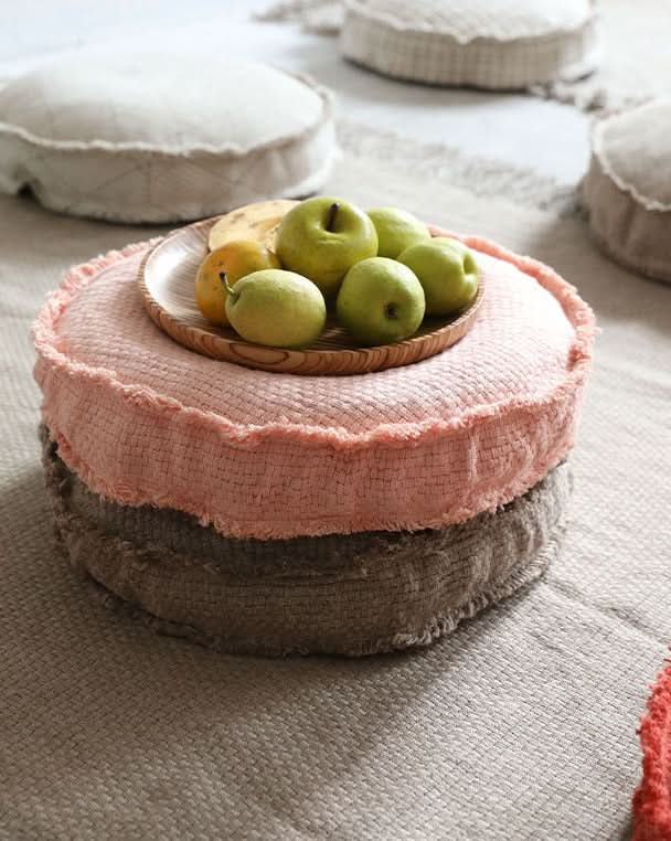 Two customizable textured floor cushions, pink and grey, with fruit on top.