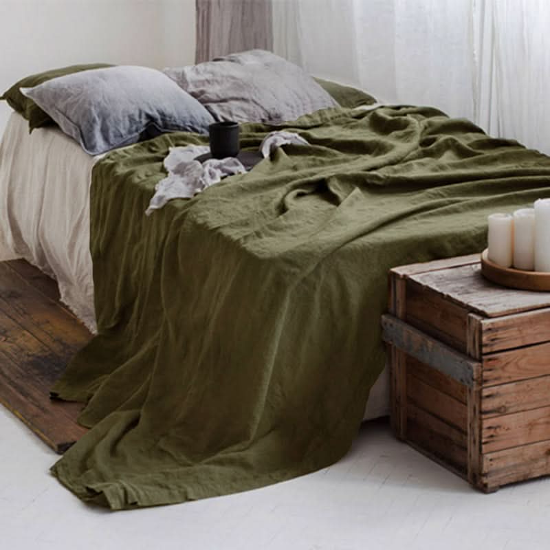 Olive green linen bed sheets draped on a bed with grey pillows, rustic decor.