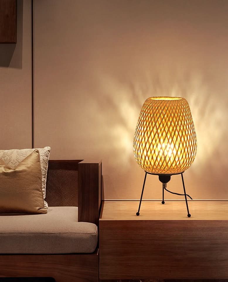 Warm rattan table lamp with intricate woven design on a wooden table, casting soft light.