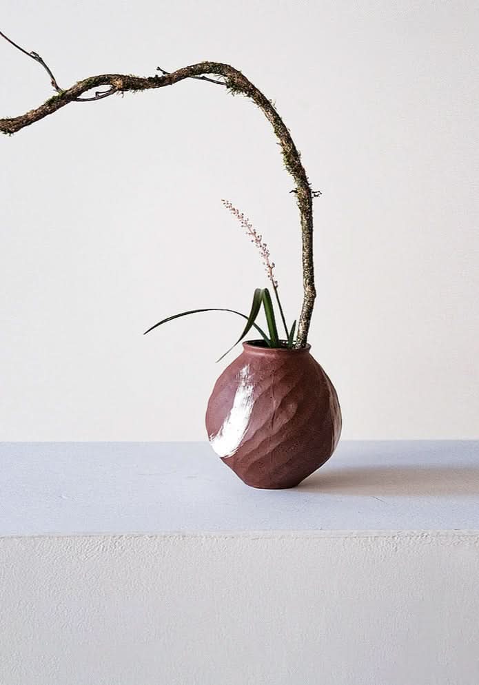 Brown vase with brushed stroke detail, holding a branch and plant. Home decor.