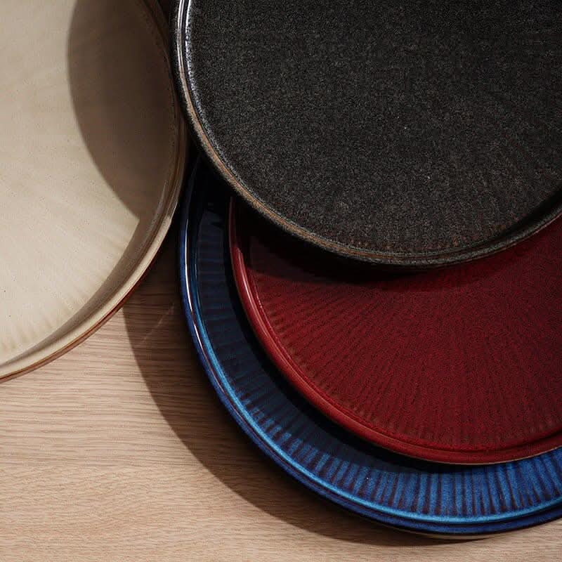 Flat Ceramic Glazed Plates in cream, charcoal, red, and blue on a wooden table.