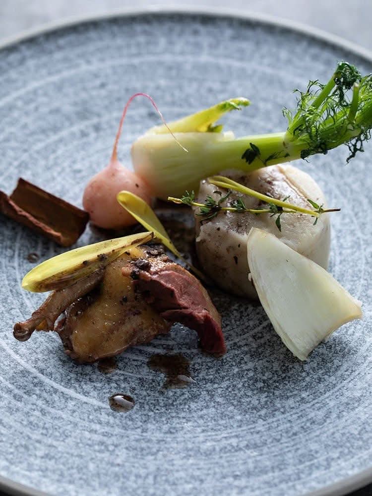 Grey speckled stoneware plate with gourmet quail dish and fresh vegetables