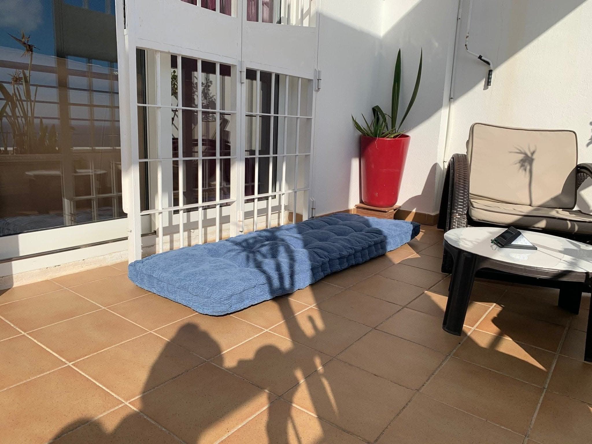 Blue corduroy custom window seat cushion on tiled patio with outdoor furniture and potted plant.