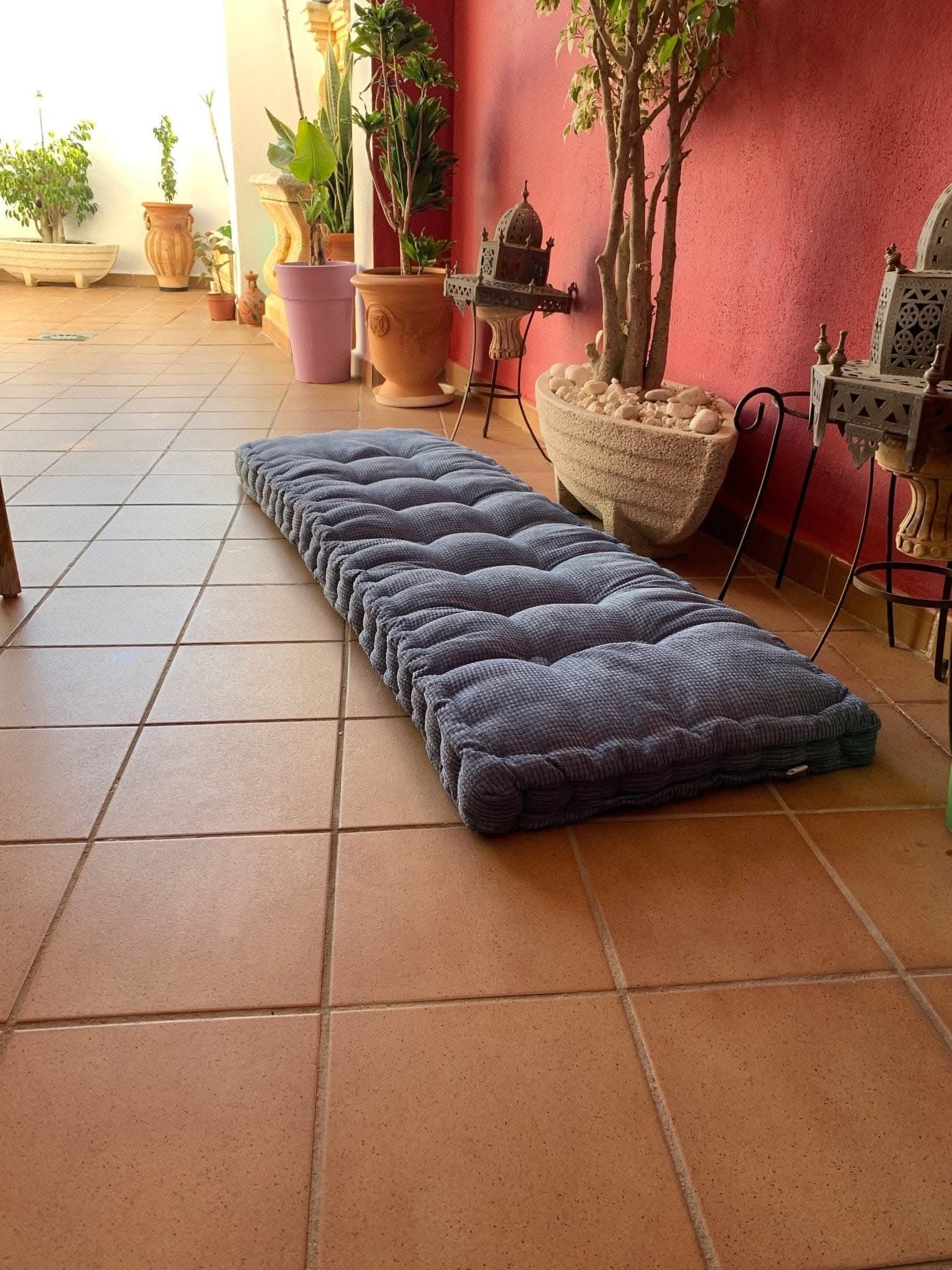 Tufted dark grey custom window seat cushion on terra cotta tile patio with plants.