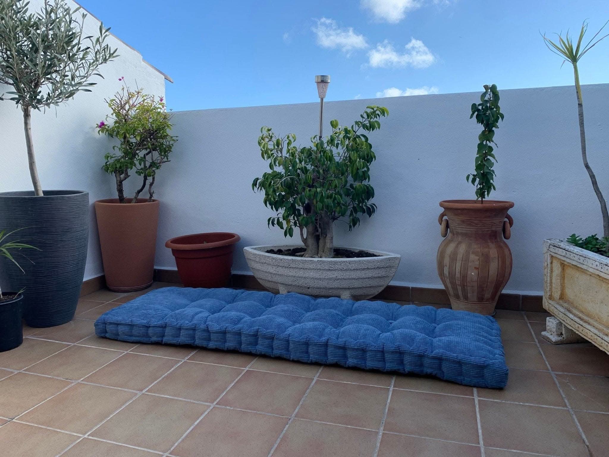 Tufted blue custom window seat cushion on tiled patio with potted plants.