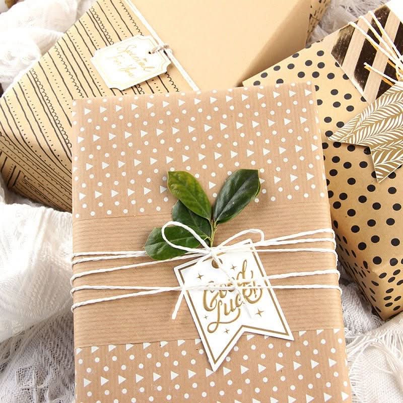 Brown gift paper with white dots & triangles, tied with twine, green leaves, & "Good Luck" tag.