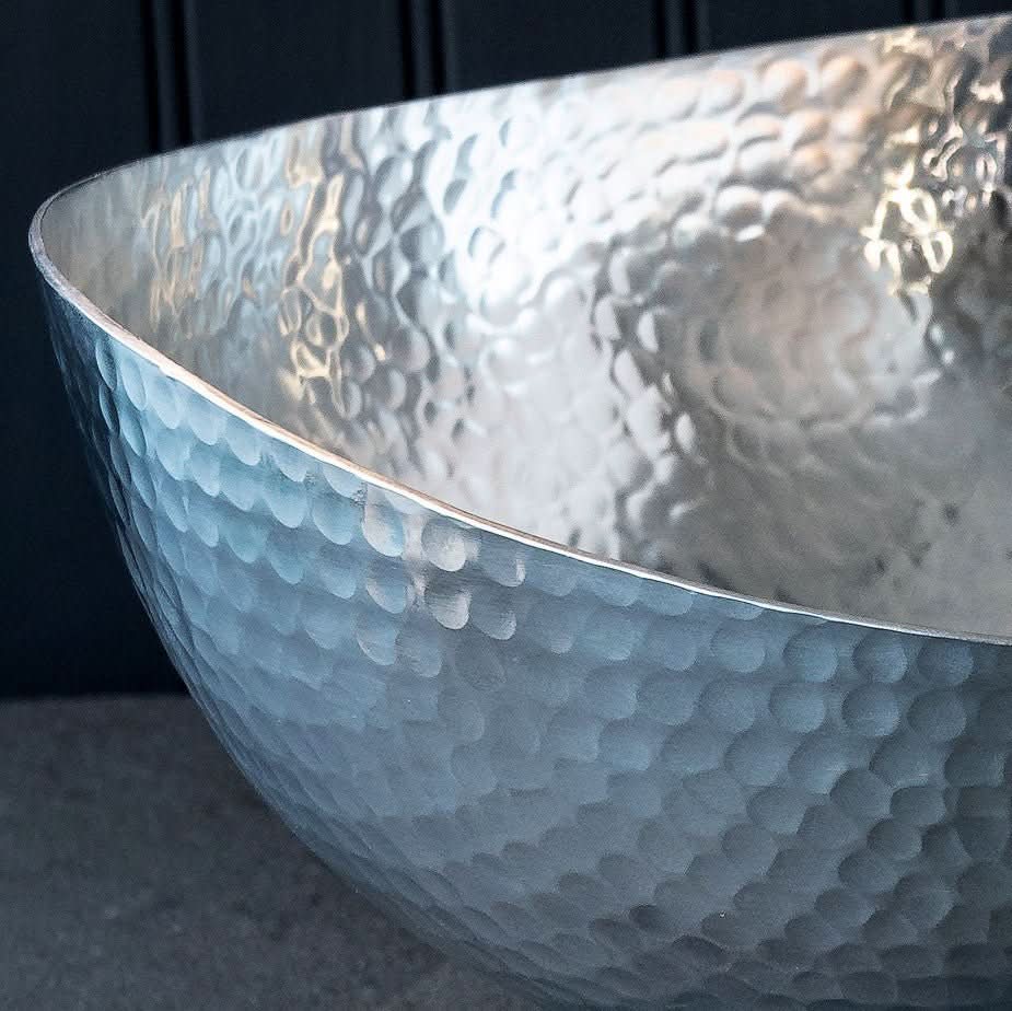 Handcrafted 12" hammered stainless steel centerpiece bowl with a reflective finish on a dark background.