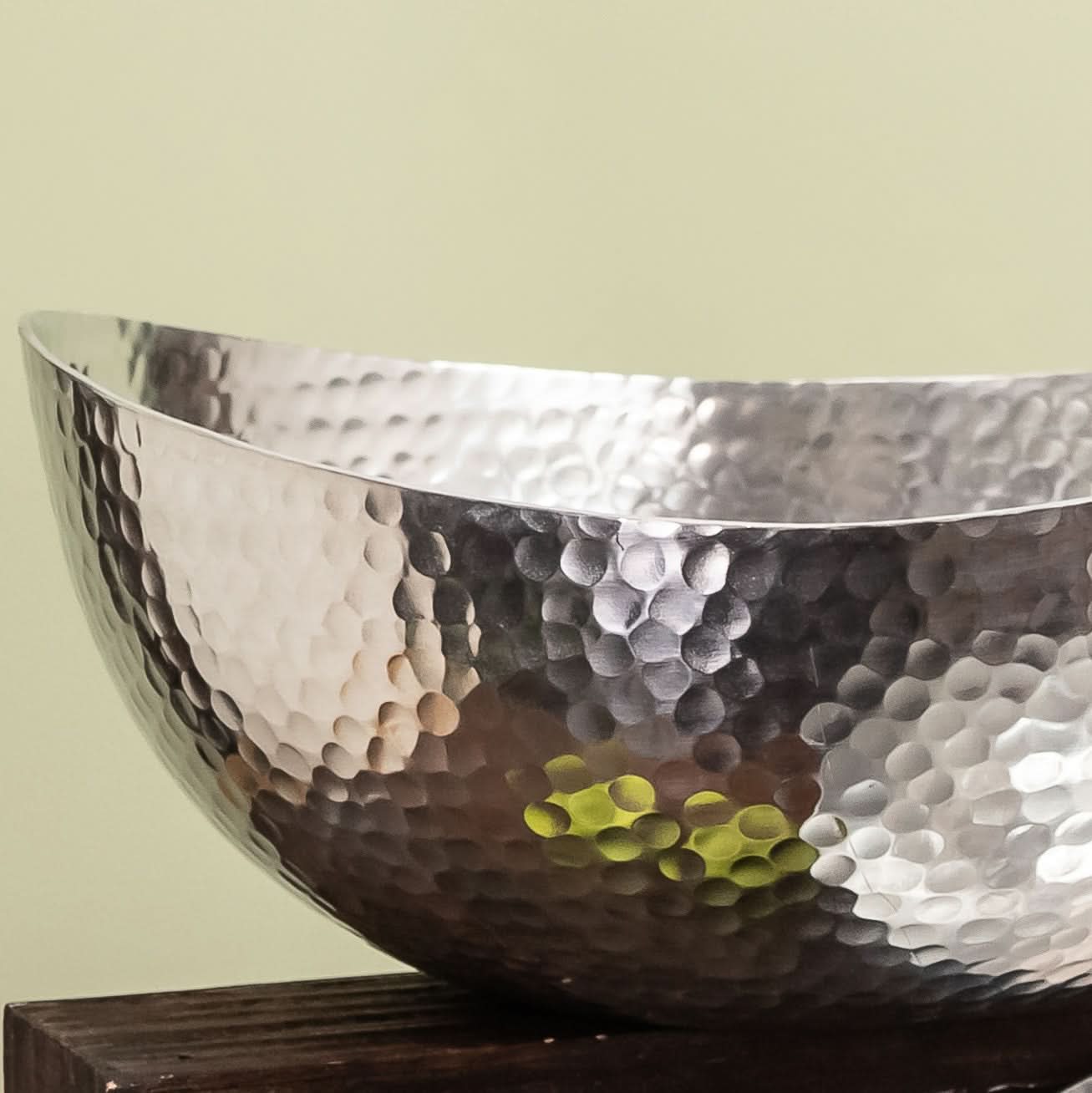 Hammered stainless steel centerpiece bowl reflecting green hues. Handcrafted home decor.