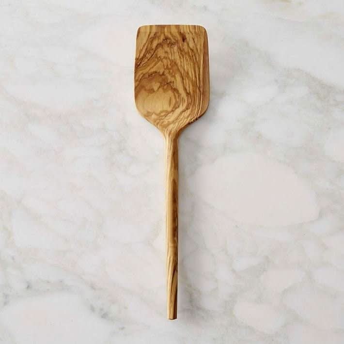 Natural wood olive spoon with handle on marble background. Spaghetti fork wooden utensil.