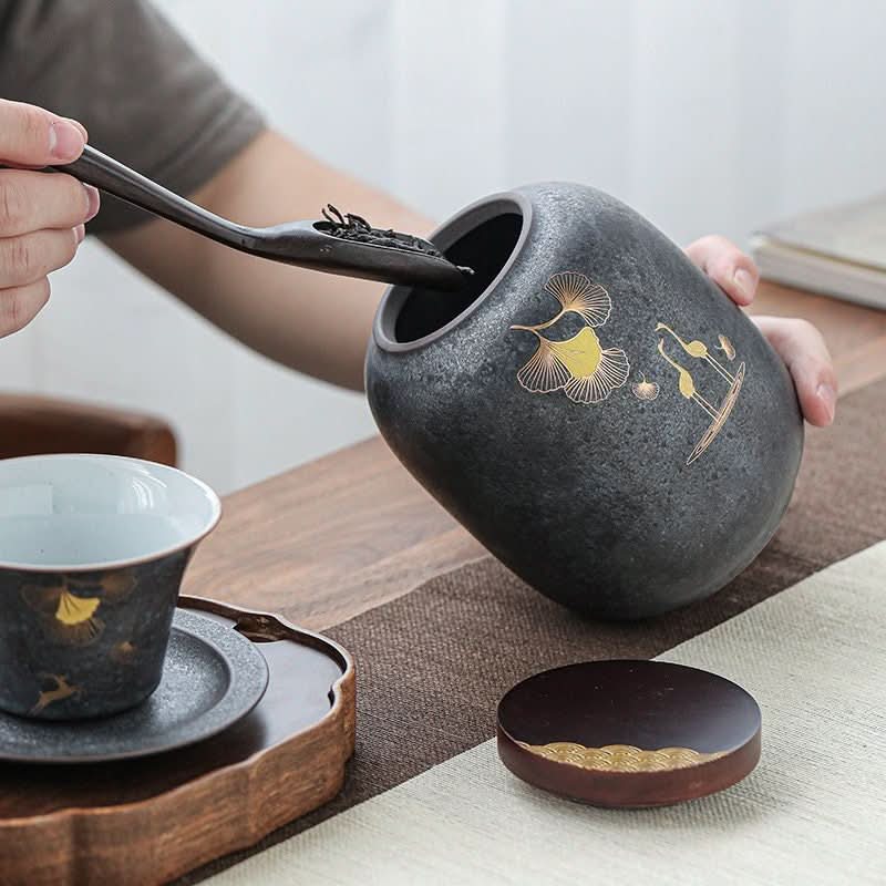 Dark grey stoneware tea caddy with gold ginkgo leaves, used for storing tea.