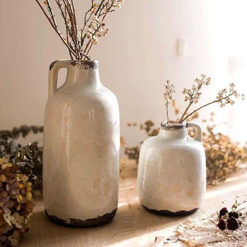 Two white ice cracked glazed mouth pottery vases with dried florals on a wooden table.