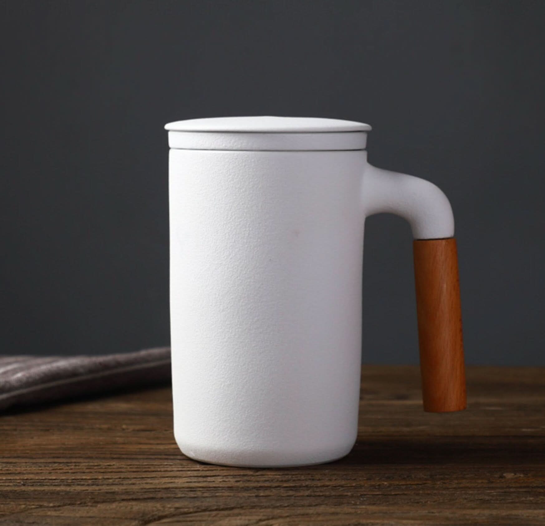 White ceramic Japanese mug with lid, strainer, and wood handle on rustic table.