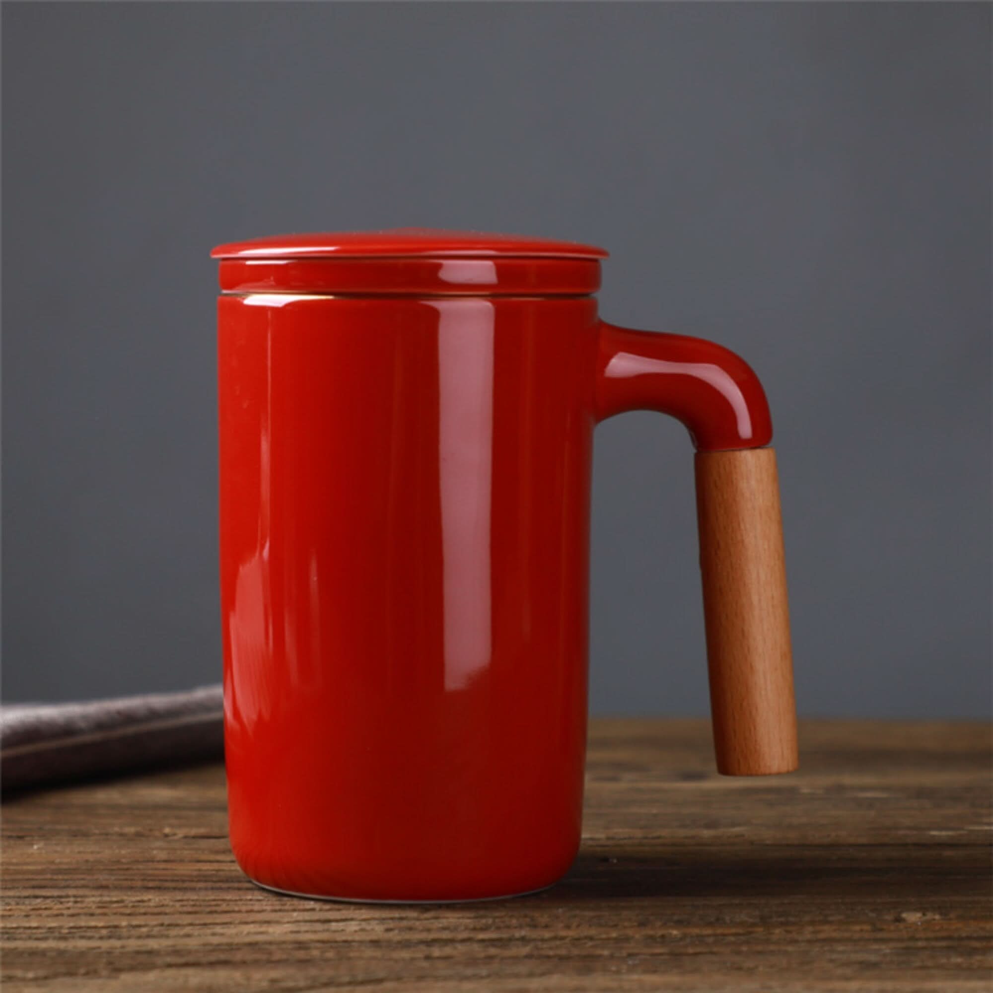 Red Japanese mug with wood handle, lid & strainer on rustic table.