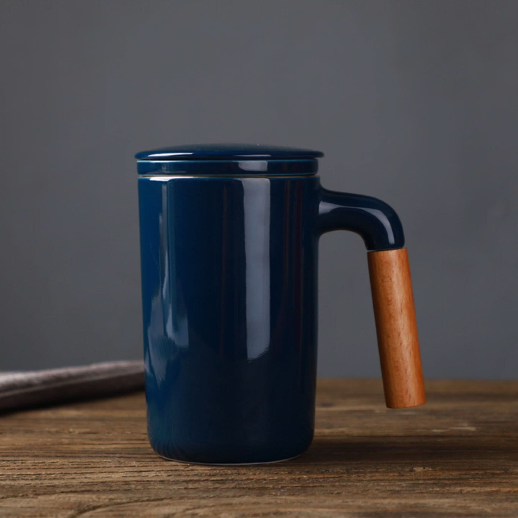 Dark blue ceramic Japanese mug with wooden handle and lid on rustic wood.