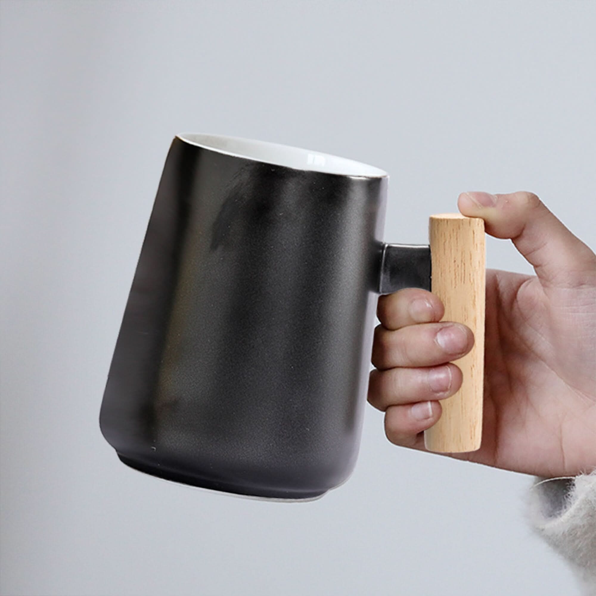 Minimalist Japanese Mug 480ml in black ceramic with a light wood handle, held by hand.