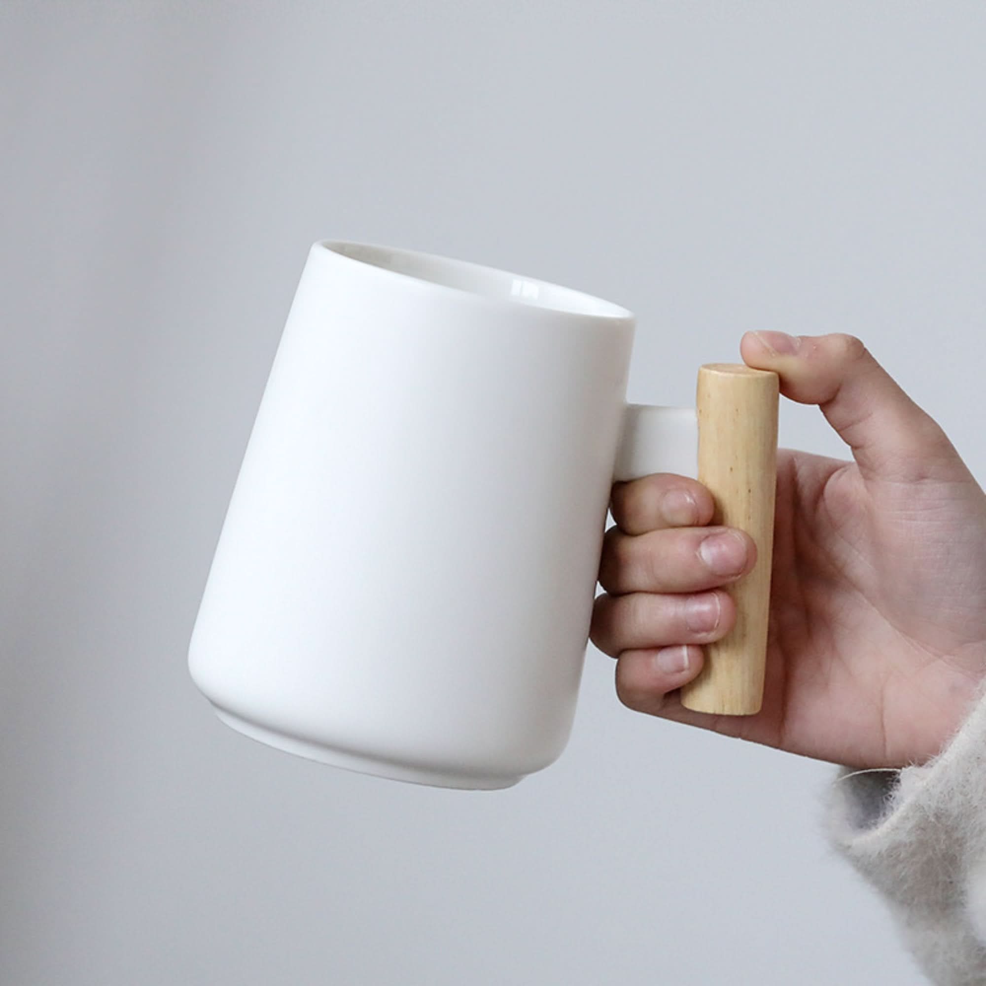 Minimalist Japanese Mug 480ml with a natural wood handle, held against a soft gray background.