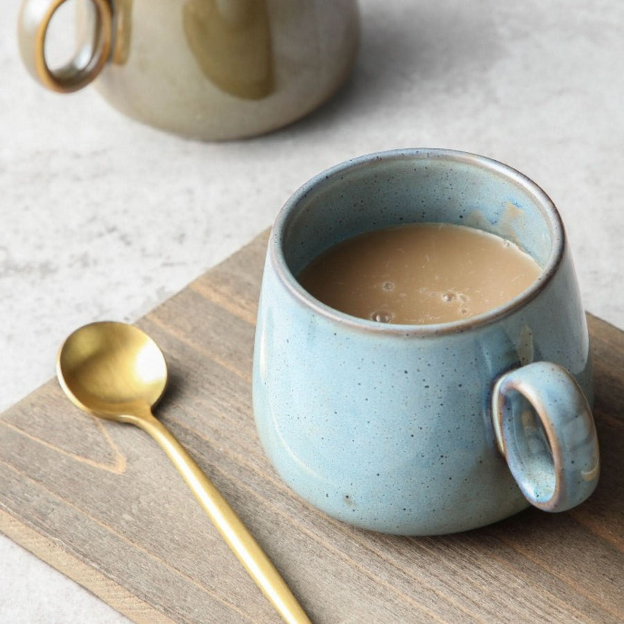 Blue stoneware Retro Mug 2 for 1 with latte, next to gold spoon on wood.