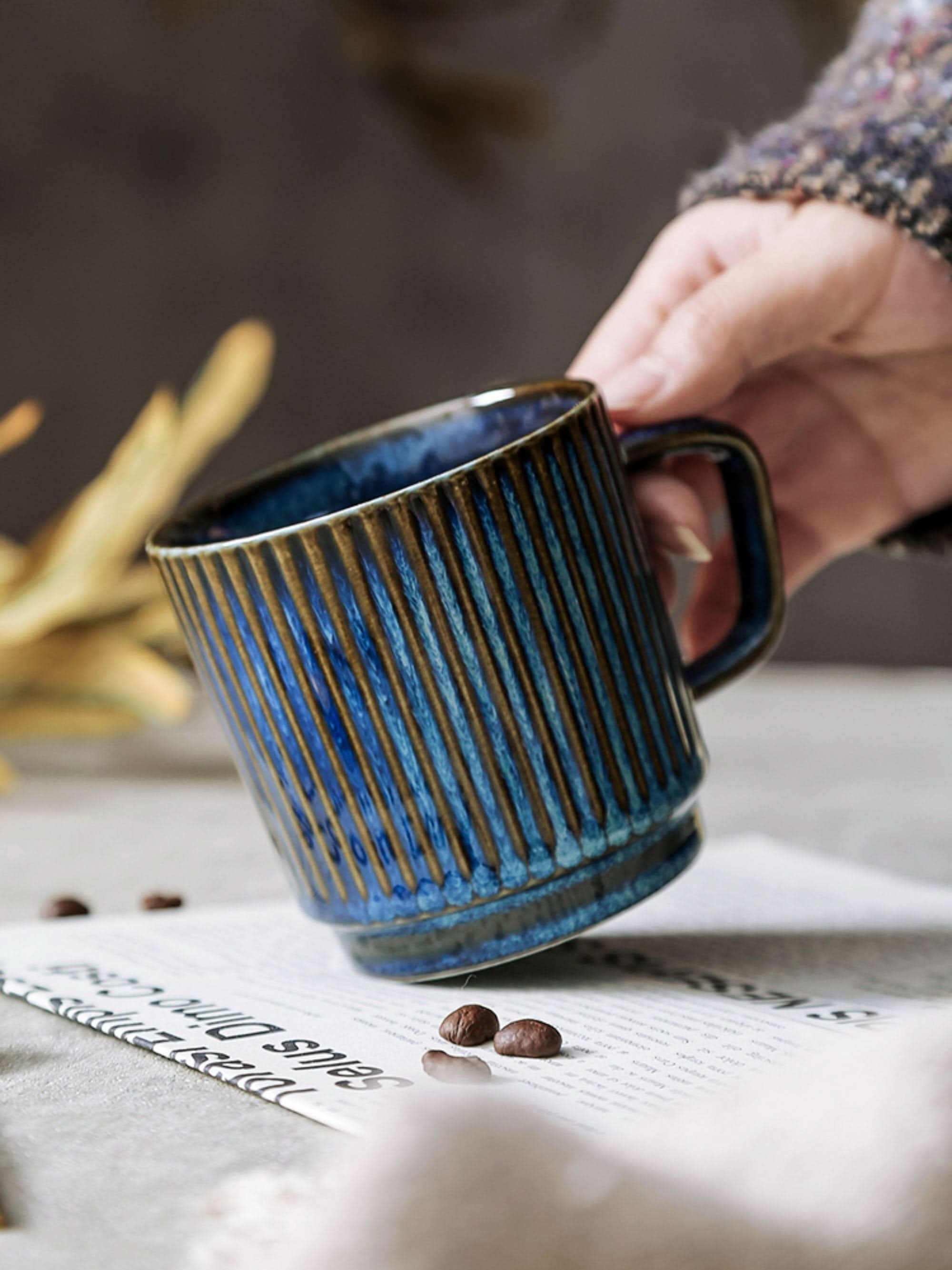 Blue glazed stoneware mug with vertical ribbed texture, held by a hand.