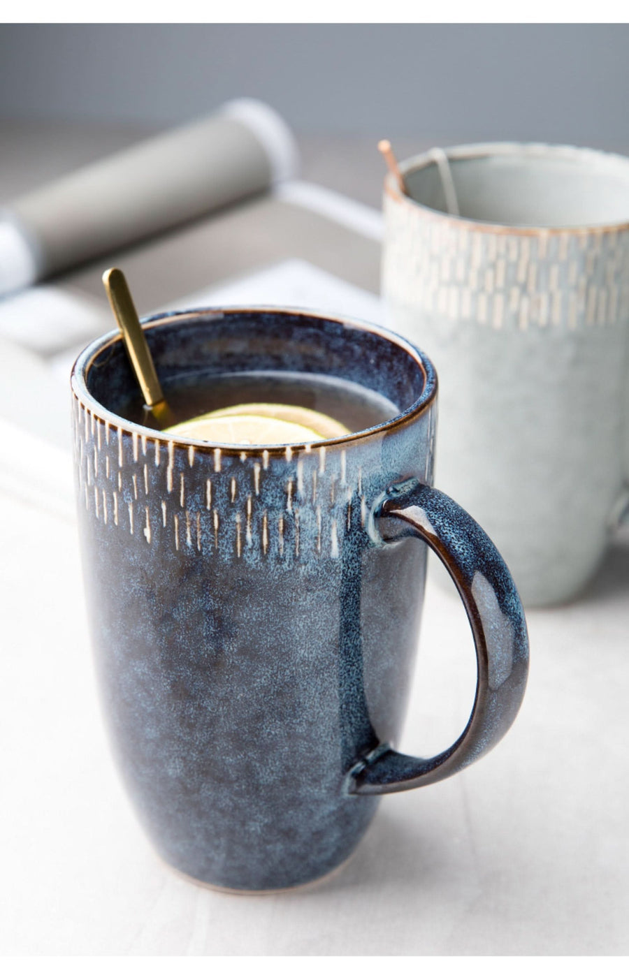 Blue glazed stoneware travel mug with gold spoon and lemon slice.