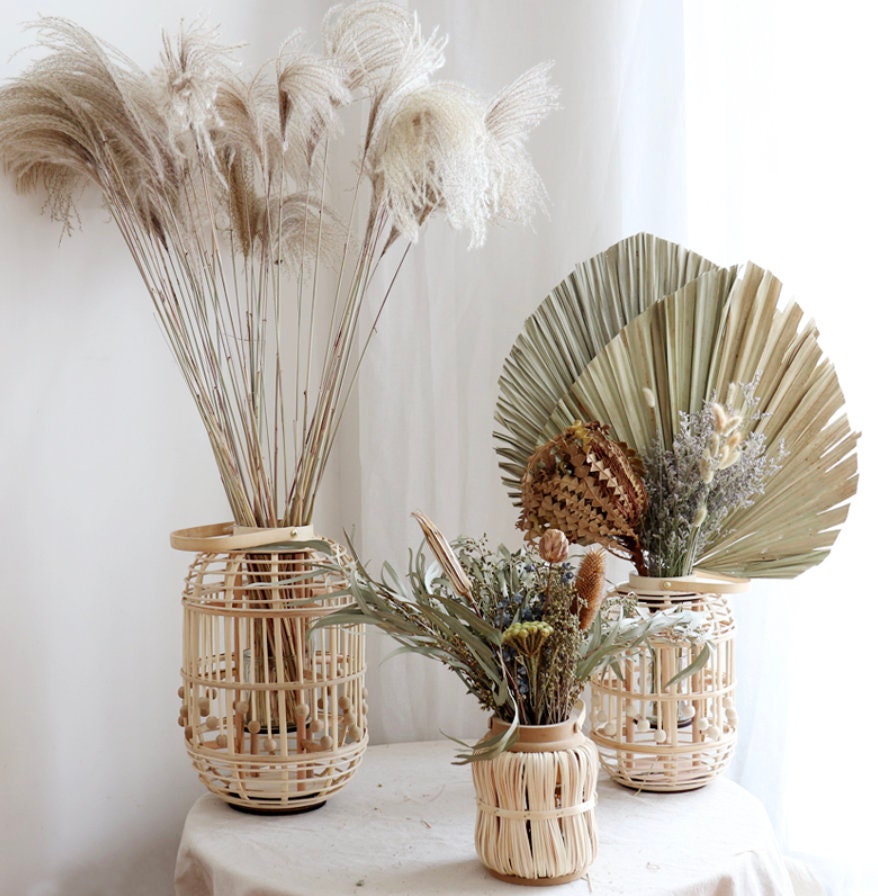 Handwoven bamboo candle holder, displayed on a table with dried flowers and plants.