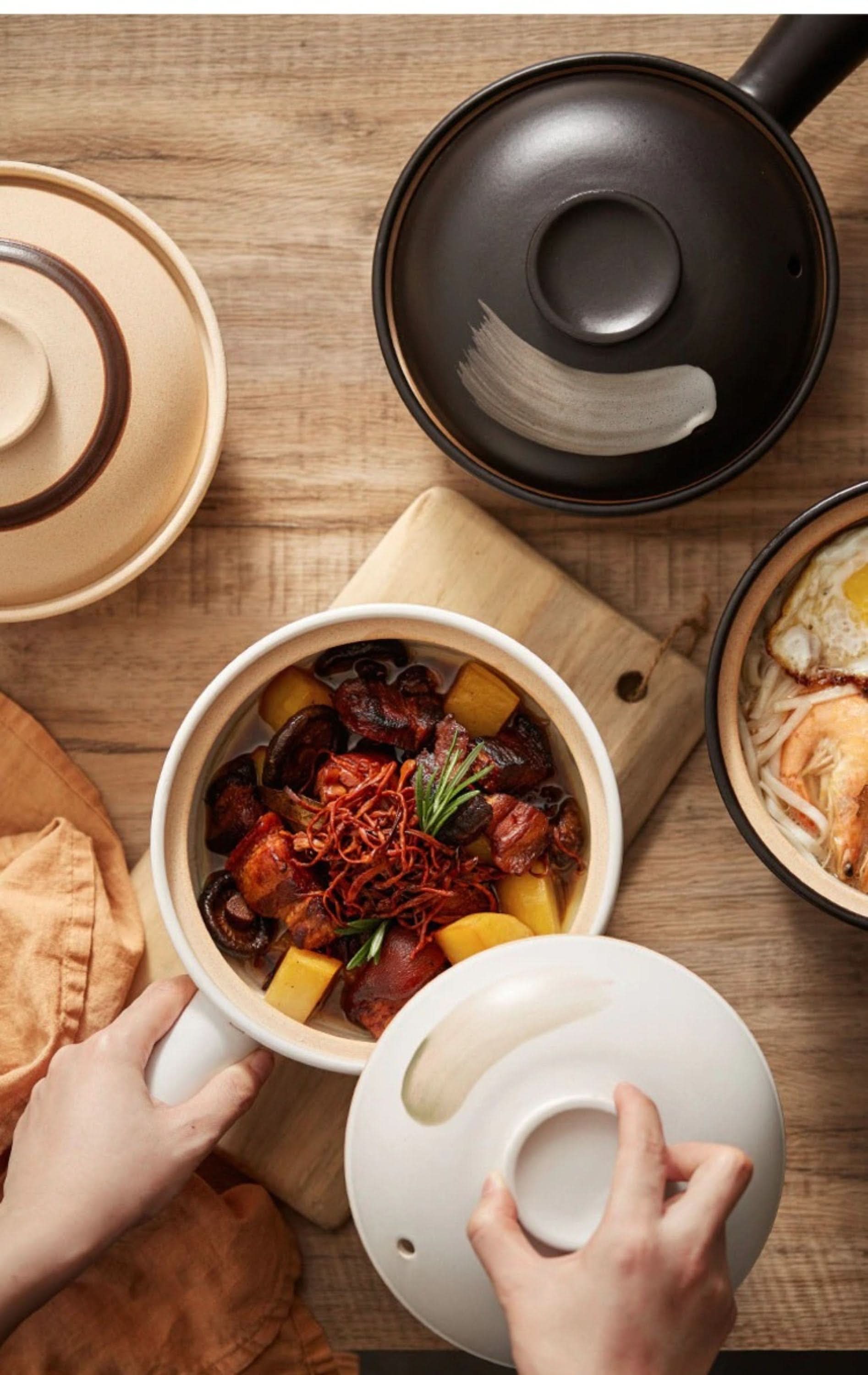 Rustic unglazed stoneware baking plates in beige and black, filled with food, on a wooden table.