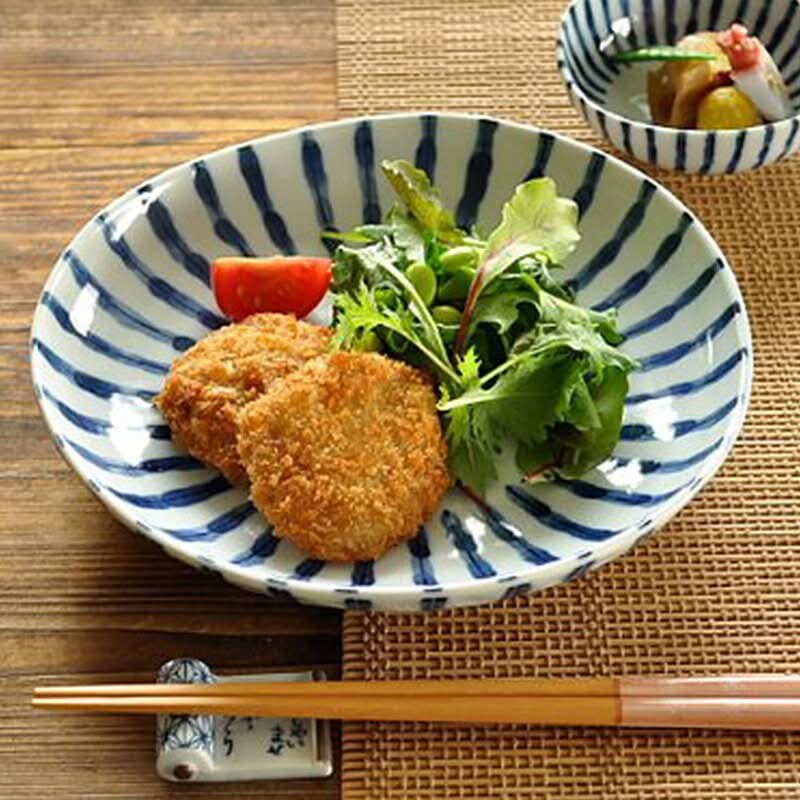 Ceramic Japanese irregular dinnerware with blue stripes holding fried food and salad.