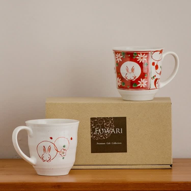 Sakura Rabbit Couple Mug Set: Hand-painted white ceramic mugs with red rabbit and floral designs, on box.