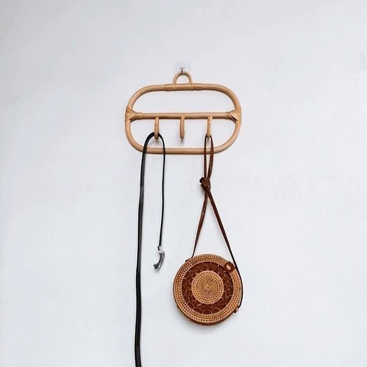 Natural rattan wall hanging hook and coat hangers with a brown circular bag and black belt on a white wall.
