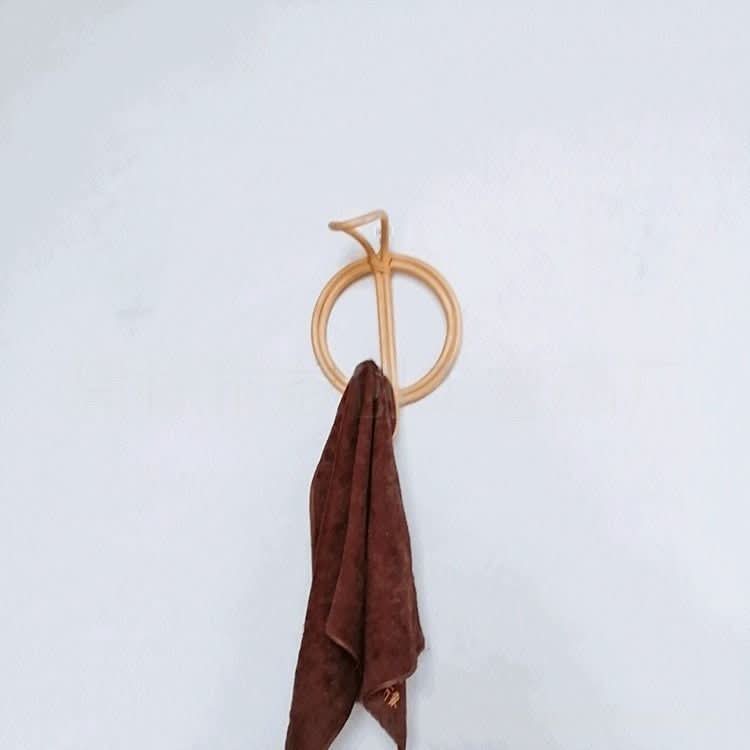 Natural rattan wall hanging hook and coat hangers holding a brown towel on a white wall.