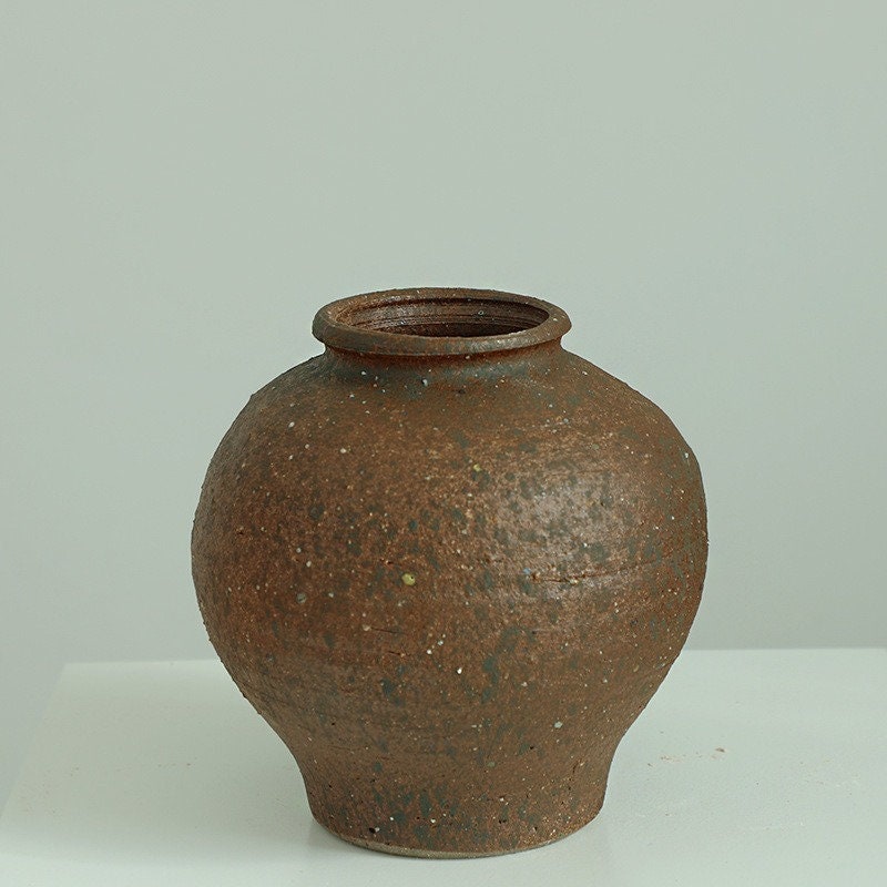 Rustic brown ceramic vase, rounded shape, tight top, textured surface.